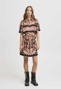 Svart klänning med ett paisleymönster i rött, rosa och guld, med knytning i midjan, korta ärmar och kombinerat med svarta blanka ankelboots.