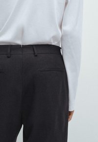 Zwarte op maat gemaakte broek met een gladde textuur, voorzien van zijzakken en een aansluitende tailleband. Gekleed met een witte longsleeve top.