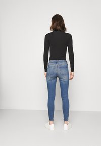 Svart långärmad topp i kombination med blå skinny jeans, med en urtvättad look, denimtextur och vita sneakers. Utsikt bakifrån.