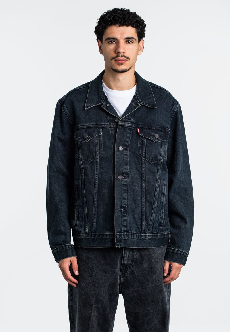 Giubbotto in denim nero con abbottonatura frontale, due tasche sul petto e colletto classico. Presenta una vestibilità rilassata e dettagli di cucitura visibili.