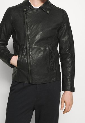 Mężczyzna noszący czarną skórzaną kurtkę z asymetrycznym zamkiem z przodu, kołnierzem z zatrzaskami oraz bocznymi kieszeniami, w połączeniu z czarnymi spodniami.