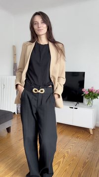Beige blejzr přes černý top, kombinovaný s černými kalhotami s vysokým pasem. Obsahuje zlatou sponu na opasku ve tvaru nekonečna. Jednoduchý, elegantní design.