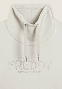 Felpa con zip beige chiaro, caratterizzata da un collo alto, cordini e logo "FREDDY" embellito in grigio con dettagli in borchie. Texture morbida.