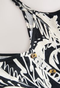 Črno-bela abstraktno vzorčasta brezrokavnik s dvema rjavima gumboma ob sprednji robu izreza na vratu.