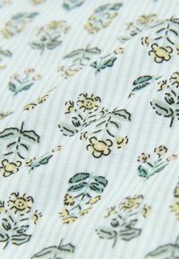 Weißer strukturierter Stoff mit kleinen gelben und grünen Blumenmustern, die diagonal angeordnet sind.