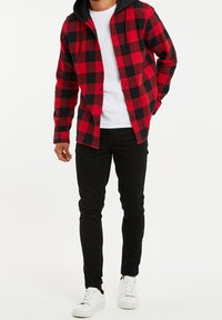 Rood en zwart geblokt flanellen shirt met een zwarte capuchon, gedragen over een wit t-shirt, in combinatie met zwarte jeans en witte sneakers.