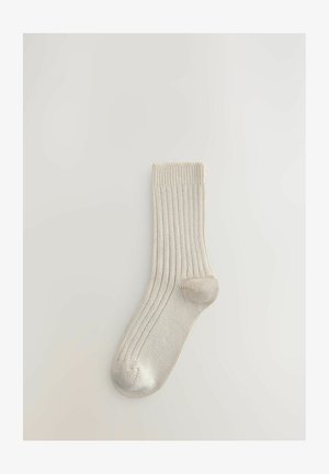 Calcetín de color beige claro con textura suave, que presenta un talón y punta reforzados, y un puño doblado.