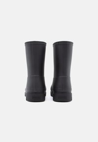 Black rubber boots with a smooth, matte finish feature a rounded shape, textured vertical lines, and a logo at the heel.