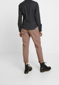 Černá košile na knoflíky vyrobená z texturované tkaniny, kombinovaná s světle hnědými kostkovanými kalhotami a černými šněrovacími botami.