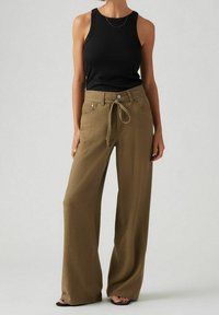 Pantalones holgados de color verde olivo con cintura ajustable, combinados con una blusa negra sin mangas. Tejido suave con un corte relajado.