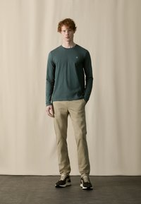 Langærmet grøn bomuldsbluse med rund hals, parret med beige tapered bukser og brune sneakers med lyse accenter.