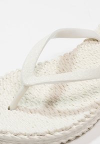 Witte flip-flops met een gemêleerd geweven zool en doorschijnende, glinsterende banden. Het ontwerp legt de nadruk op een eenvoudige, lichte constructie.