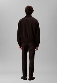 Chaqueta bomber negra con cuello alto, tela texturizada y dobladillo elástico. Combinada con pantalones negros a juego y zapatos sin cordones.