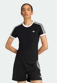 Camiseta negra con detalles blancos, cuello redondo acanalado y tres rayas blancas en cada hombro. Presenta un pequeño logo en el pecho.