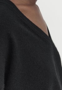 Black knitted sweater with a V-neckline. Soft texture, slim fit, and ribbed detailing along the neckline and hem.