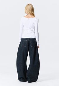 Pantaloni in denim a gamba larga con lavaggio scuro, vita alta e due tasche posteriori. Top bianco a maniche lunghe con scollo rotondo e design aderente.