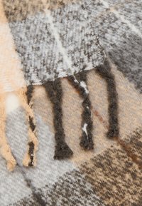 Écharpe en mélange de laine avec motif à carreaux beige, gris et noir. Bords avec finition à franges. Texture douce, épaisseur moyenne, aspect chaud.
