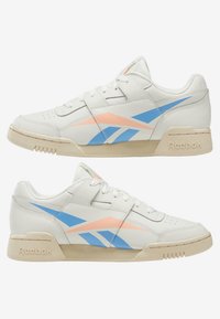 Sneakers bianche in pelle con strisce diagonali blu chiaro e pesco, suola in gomma, punta rotonda e colletto imbottito. Presentano il logo Reebok sul tallone.