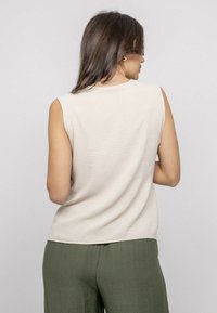 Haut sans manches beige clair en tissu texturé, avec un col rond et une coupe décontractée, associé à un pantalon vert ample.