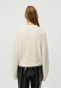 Un pull en crème, duveteux, avec une coupe ample, un col rond et des manches longues, associé à un pantalon noir brillant.