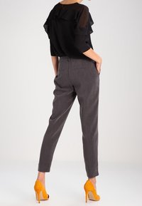 Czarna bluzka z szyfonu z falbanistymi rękawami w połączeniu z szarymi spodniami w kant i jasnymi żółtymi szpilkami, widok z tyłu.