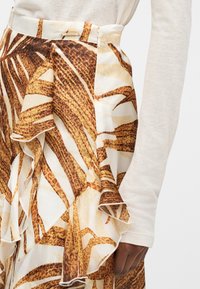 Φούστα με ψηλή μέση, με στρώματα βολάν και animal print σε καφέ, πορτοκαλί και κρεμ αποχρώσεις, φορεμένη με ανοιχτό μπεζ μακρυμάνικη μπλούζα.