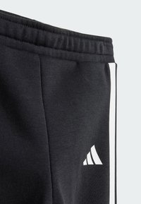Pantalones deportivos negros hechos de una tela suave con una cintura acanalada, que cuentan con franjas laterales blancas y un pequeño logo blanco en la parte inferior de la pierna.