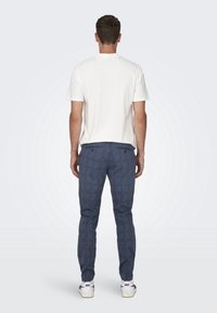 T-shirt blanc à manches courtes associé à un pantalon à carreaux bleu foncé et des baskets blanches. La tenue a une coupe décontractée et relaxée.