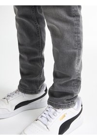 Jeans grises ajustados con un acabado texturizado y costuras laterales, combinados con zapatos blancos con acentos negros y un logo dorado.