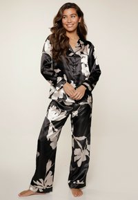 Ensemble de pyjama en satin noir avec des motifs floraux blancs, un haut à boutons avec col et un pantalon ample à drapé élégant.