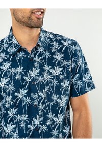 Maglietta a maniche corte con bottone in tessuto blu scuro con stampa di palme bianche. Il design è completato da un colletto classico e bottoni discreti.