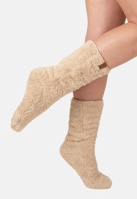 Calze beige, soffici, con una superficie testurizzata e una parte superiore a coste. Presentano un piccolo etichetta marrone sul lato.
