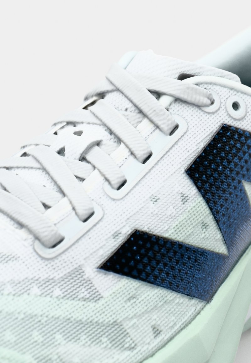 Weiße strukturierte Sneaker mit dunkelblauen geometrischen Musterakzenten, ausgestattet mit dünnen Schnürsenkeln und einer gepolsterten mintgrünen Sohle.