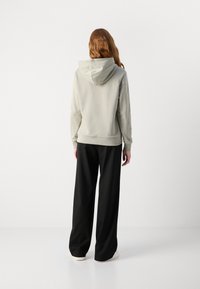 Sudadera gris clara con capucha ajustable, combinada con pantalones negros holgados y zapatillas blancas. Textura de tela suave, diseño minimalista.