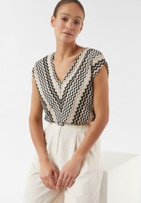 V-hals blouse van gemusterde stof met zigzagstrepen in zwart, beige en wit; korte mouwen, lichte stof en een relaxed fit.