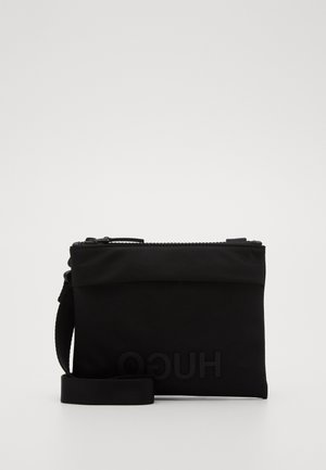 Sort rektangulær crossbody-taske med lynlåslukning, justerbar rem og diskret prægning af brandlogo på forsiden.
