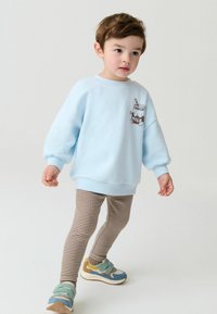 Svijetloplavi dukserica s grafikom Choco Milk, u kombinaciji s prugastim smeškim tajicama i višebojnim patikama sa trakama.