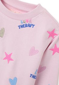 Sudadera rosa con corazones bordados en azul, rosa y plata, y el texto "TERAPIA DEL AMOR" en letras coloridas.