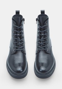 Un paio di stivali neri in pelle con lacci e cerniere laterali, mostrati frontalmente su uno sfondo bianco.