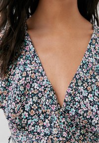 Robe fleurie avec un décolleté en V profond, fond foncé orné de petites fleurs blanches, roses et turquoise, tissu léger et texture douce.