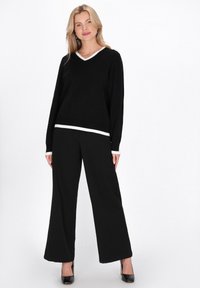 Pulover negru cu guler în V și bordură albă, asortat cu pantaloni negri largi. Ținuta are o croială lejeră și o textură netedă.