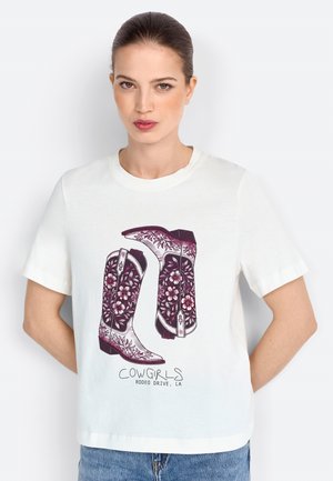 T-shirt blanc à manches courtes avec un graphique de bottes de cowboy violettes ornées de motifs floraux et le texte "COWGIRLS RODEO DRIVE, LA" en dessous.