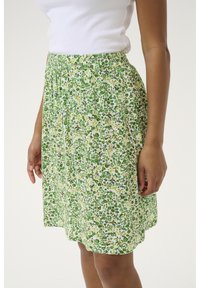 Blomsterskirt lavet af letvægtsstof, med et grønt og gult mønster. Elastisk talje med en samlet tekstur for komfort.