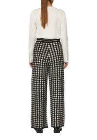 Zwart-witte geblokte wijde broek van een textuurstof met elastische tailleband, gecombineerd met een crèmekleurige blouse met lange mouwen.
