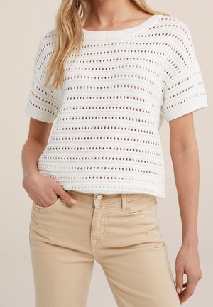 Top blanco de punto con rayas de calados, mangas cortas y un corte relajado. Combinado con jeans de color beige claro. La textura parece transpirable.