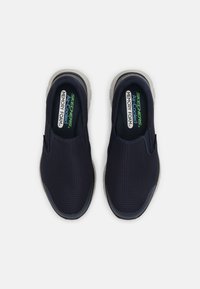 Tengerészeti slip-on cipők texturált hálós felsőrésszel, párnázott memóriahab talpbetéttel és szürke gumitalppal. Zöld és fehér színű logóval rendelkezik.