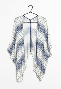 Kimono leggero in crema con motivi geometrici blu navy, con apertura davanti, maniche larghe e una vestibilità ampia; appeso a un gancio nero.