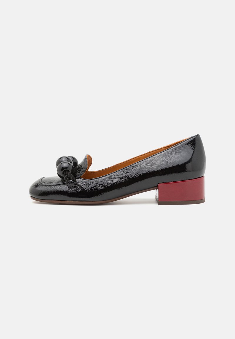 Black patent leather pump with a rounded toe, featuring a decorative knot and a square, burgundy heel. Smooth texture with subtle shine.