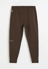 Brązowe dresowe spodnie z polaru z elastycznym paskiem w talii, bocznymi kieszeniami, ściągaczami przy nogawkach i małym logo na lewej udzie. Gładka faktura.