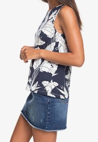Granatowy bezrękawnik z białym wzorem kwiatowym, okrągłym dekoltem i luźnym krojem, w połączeniu ze spódnicą mini z denimu z postrzępionym dołem.